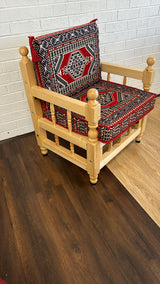 Red palace floor cushion set with ornate patterned red cotton cover on a rustic wood chair in a traditional majlis