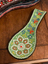Light green spoon holder on a kitchen counter with a wooden spoon laid across its handpainted ceramic surface